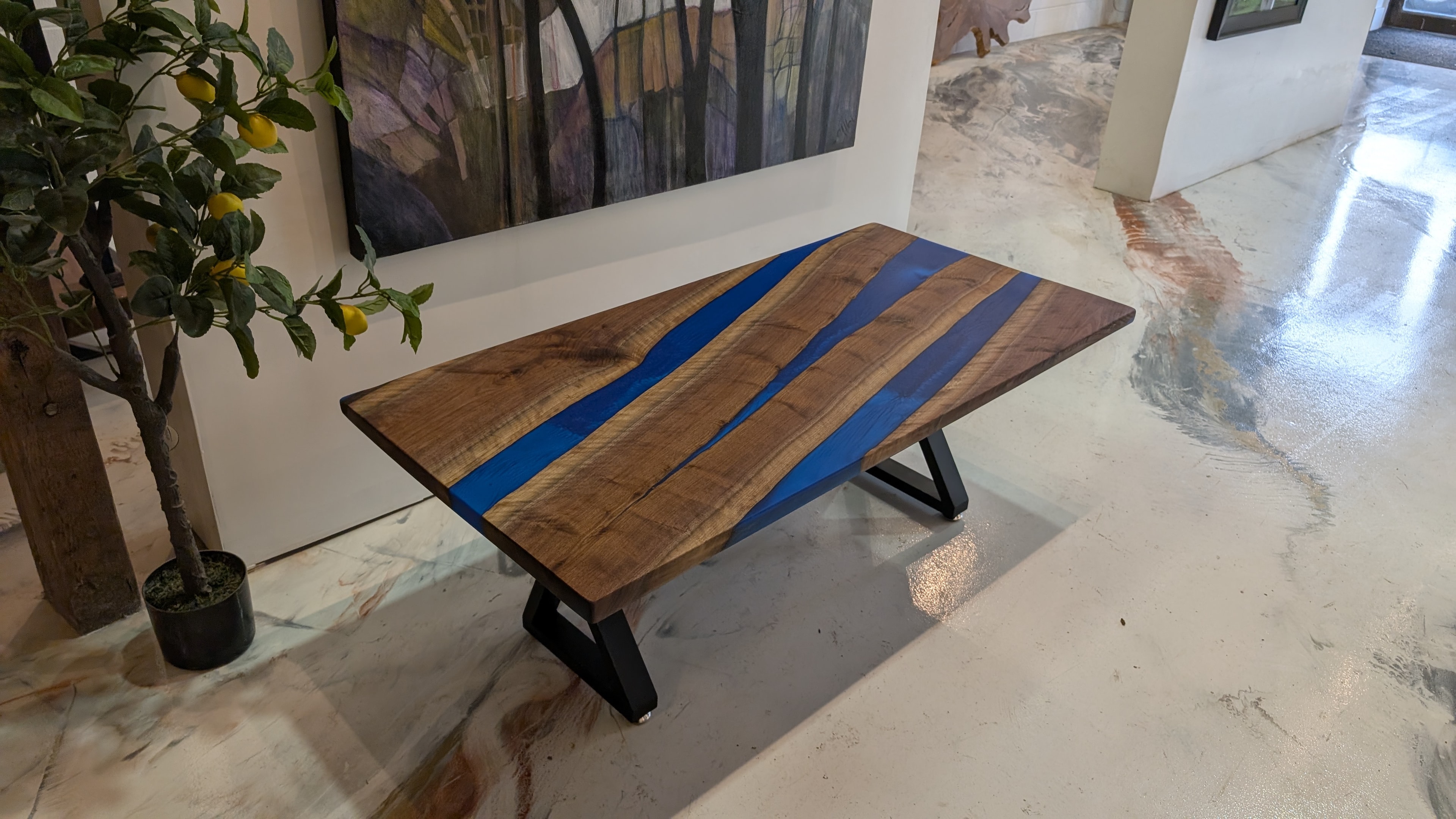 Live edge walnut triple blue epoxy river coffee table with A-frame base displayed in art gallery