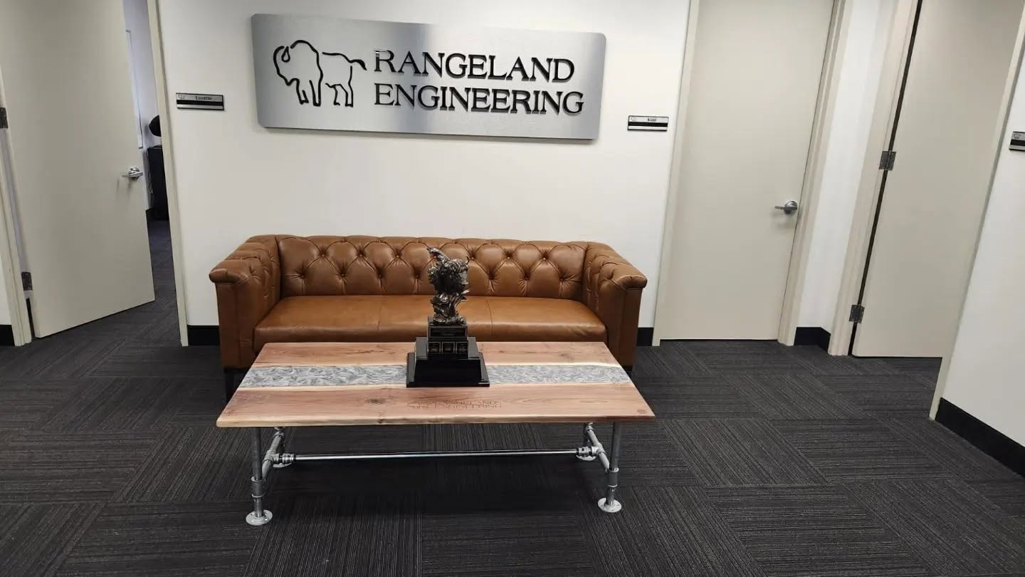 Custom elm coffee table with clear epoxy river inlay and industrial pipe legs — installed at Rangeland Engineering Calgary office lobby