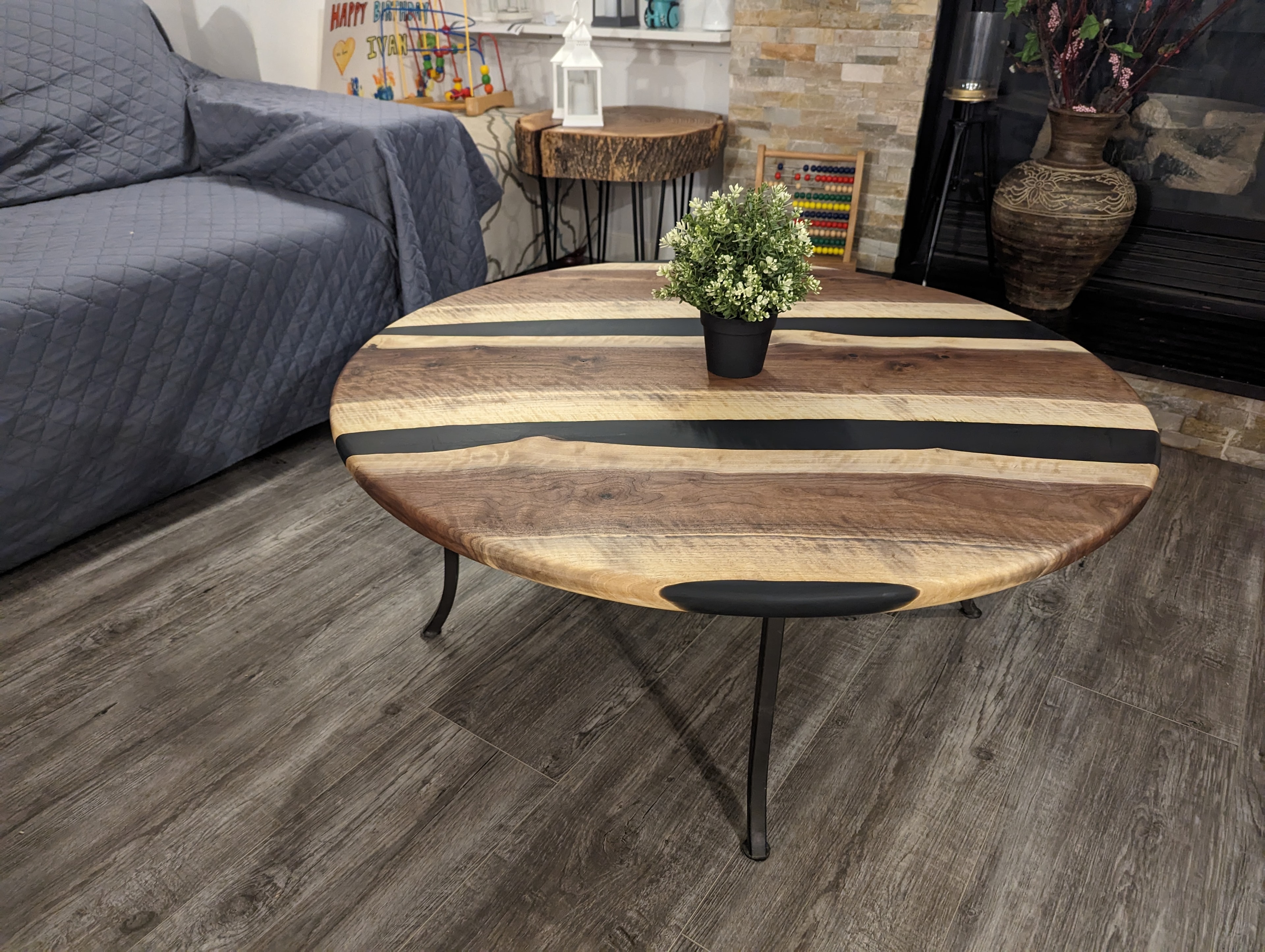 Round walnut black epoxy river coffee table with hairpin legs beside stone fireplace