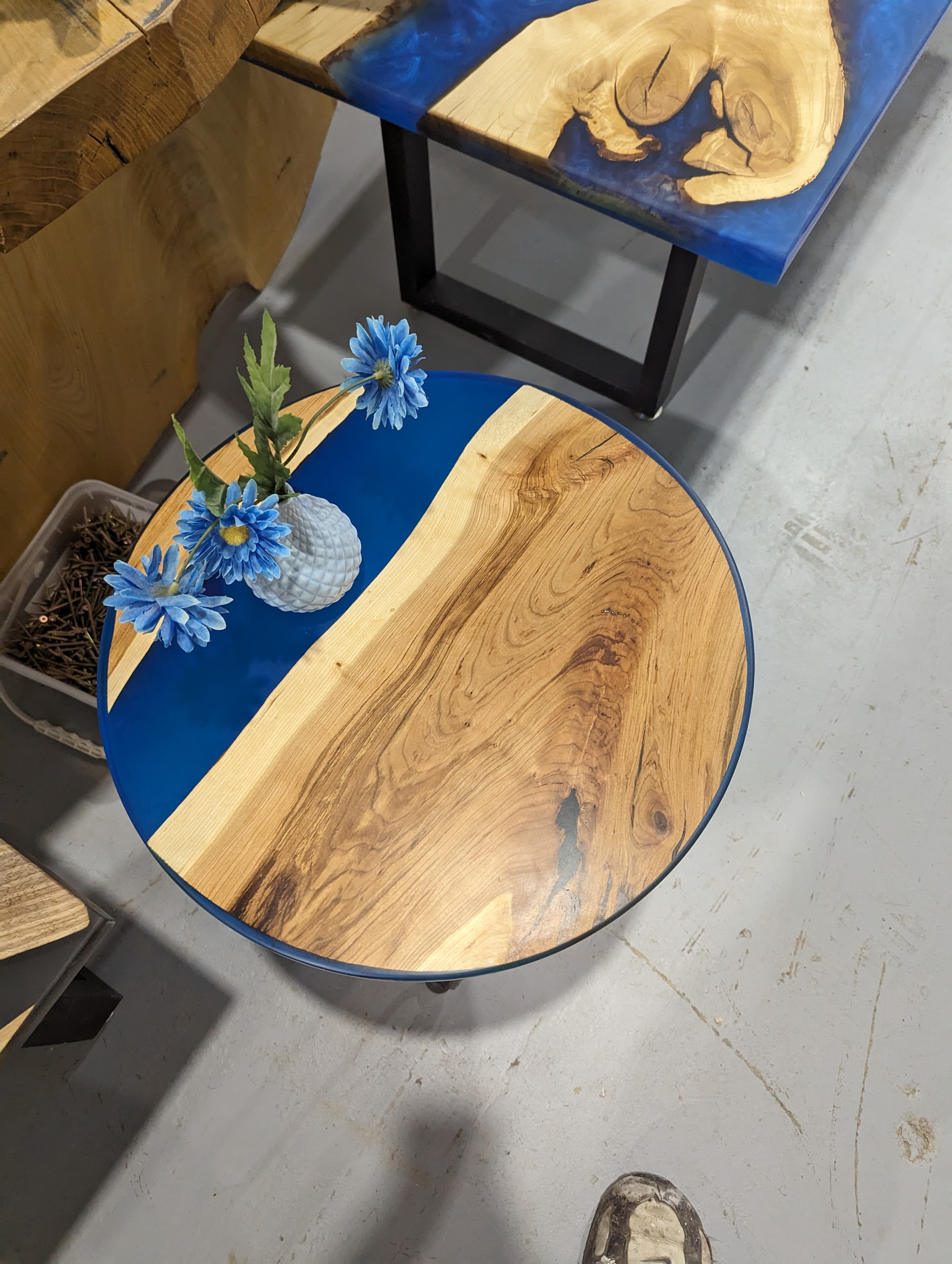 Round elm blue epoxy coffee table overhead view in shop — bold blue river edge detail
