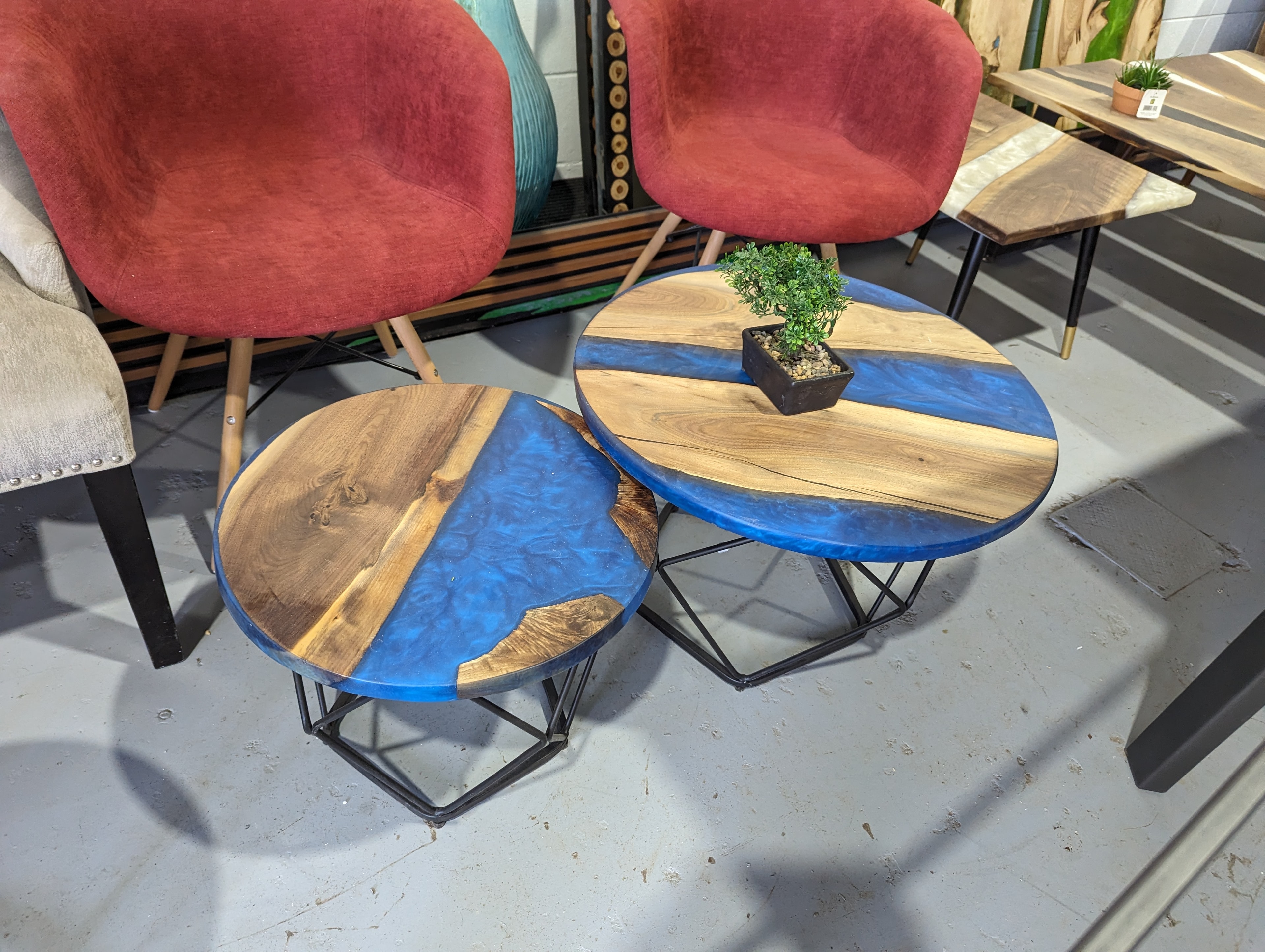 Round walnut blue epoxy nesting coffee table set in shop display with red velvet chairs