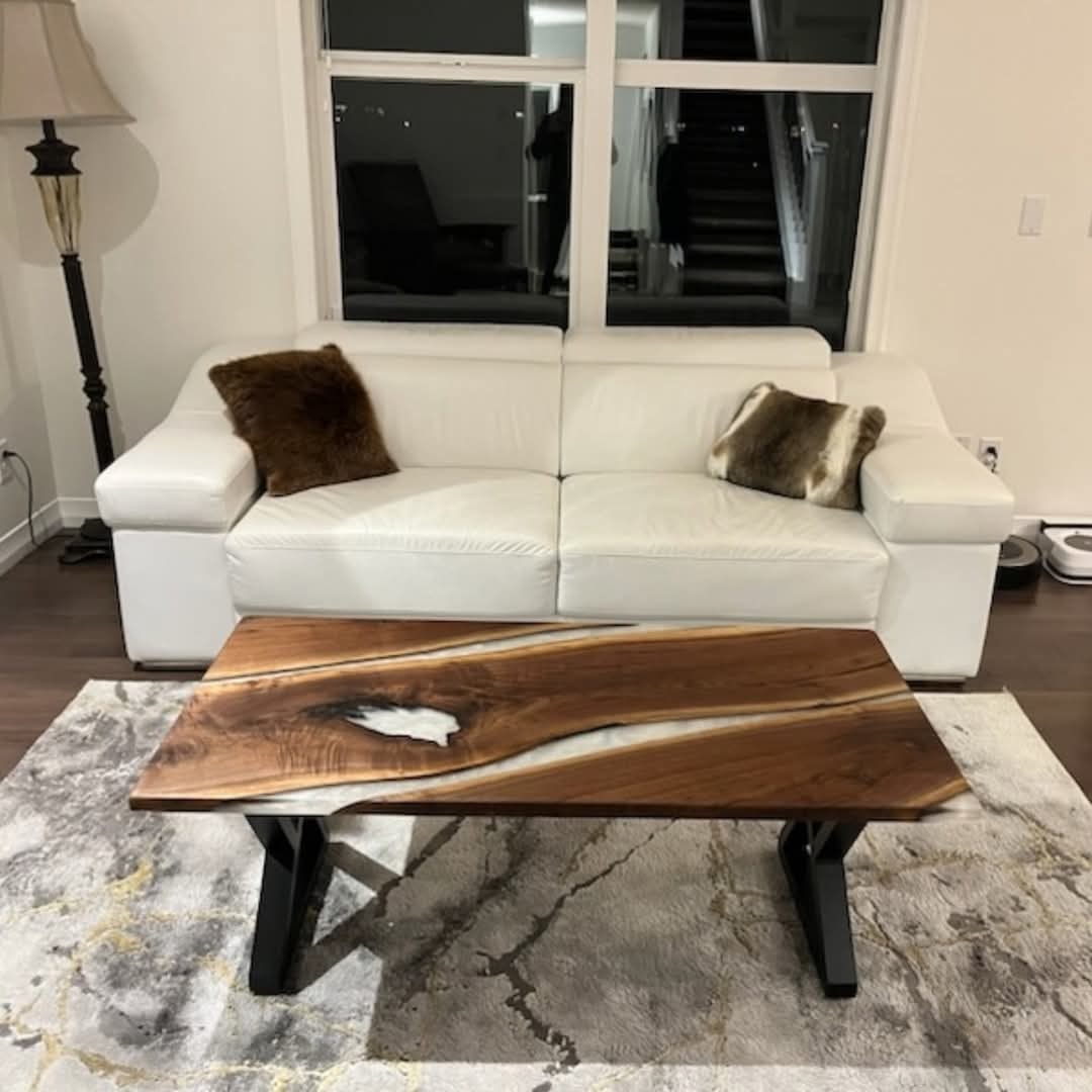 Live edge walnut white epoxy river coffee table with black A-base in front of white leather sofa