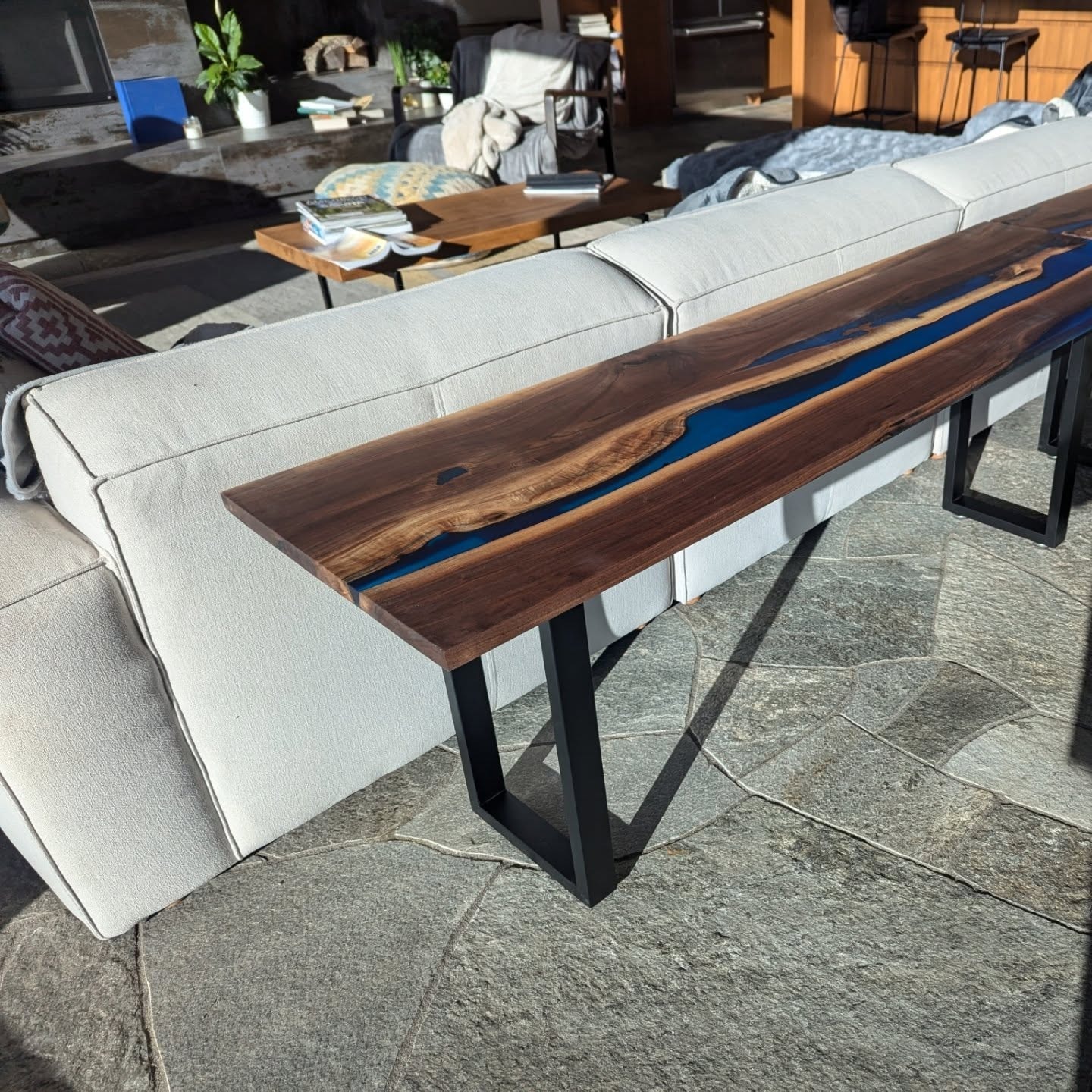 Live edge walnut blue epoxy couch table with black U-base on stone patio
