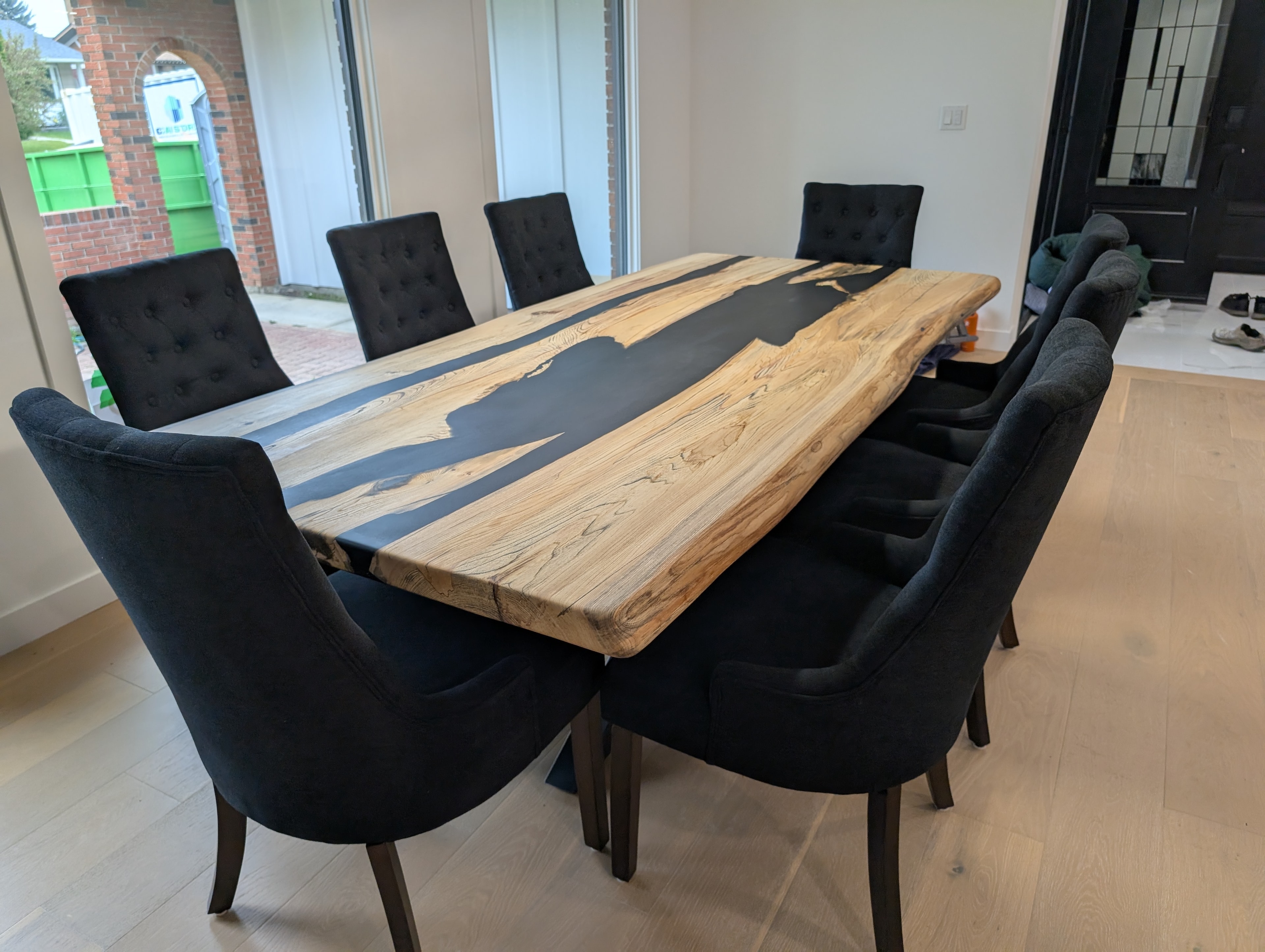 Black epoxy river dining table with elm slabs and dark tufted chairs
