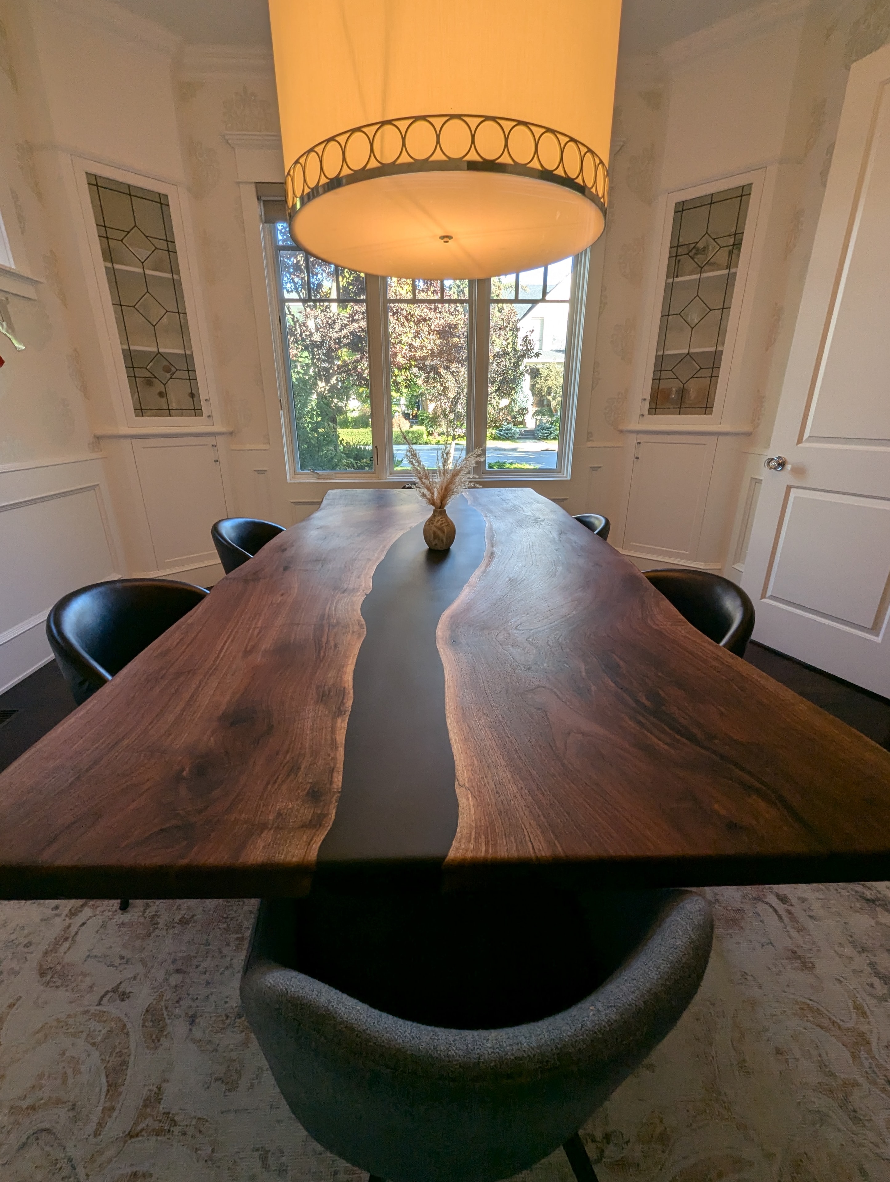 Black epoxy river walnut dining table in formal dining room with bay window and chandelier