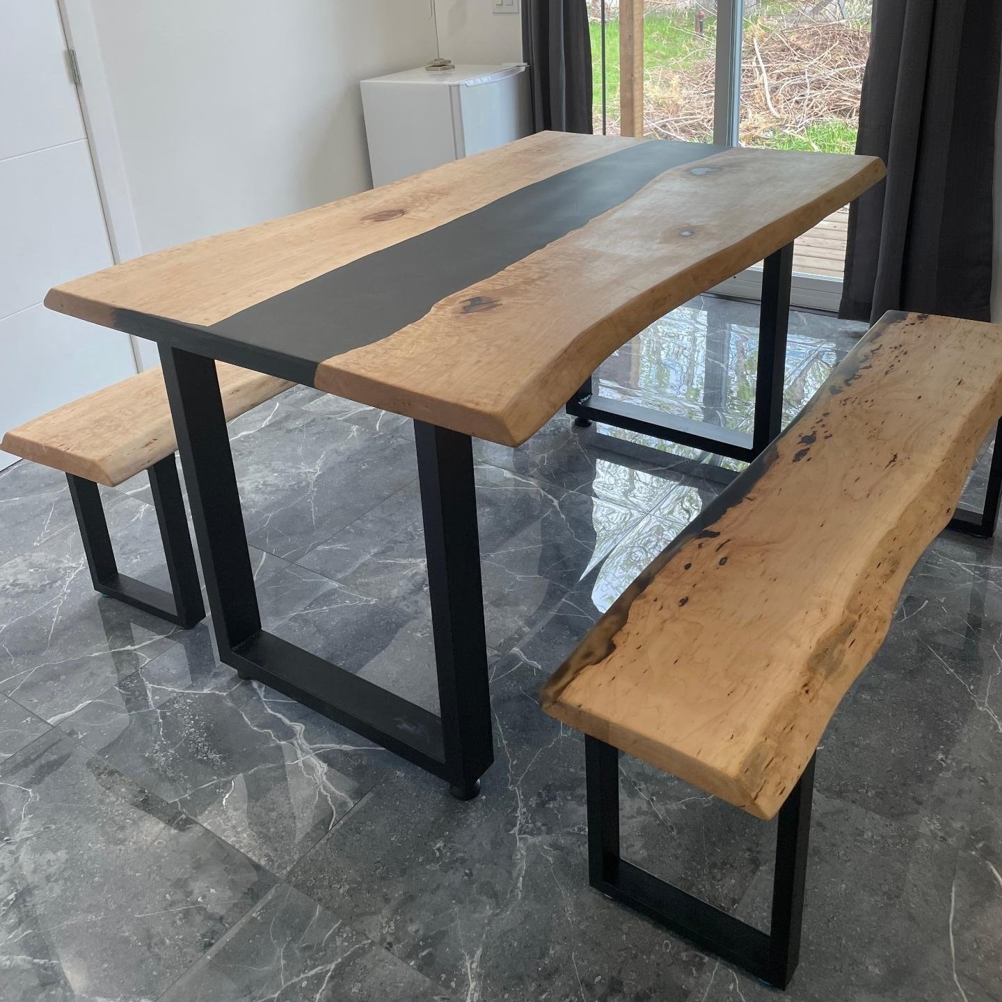 Live edge maple black epoxy river dining table with matching benches on marble floor