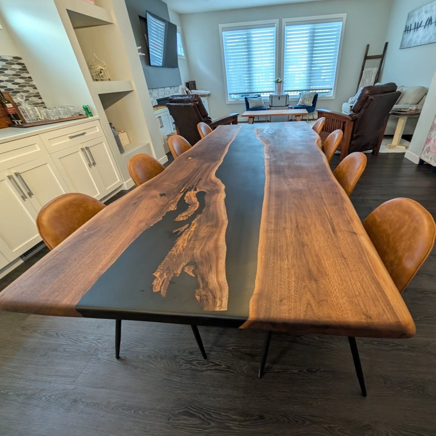Live edge walnut black epoxy river dining table with tan leather barrel chairs