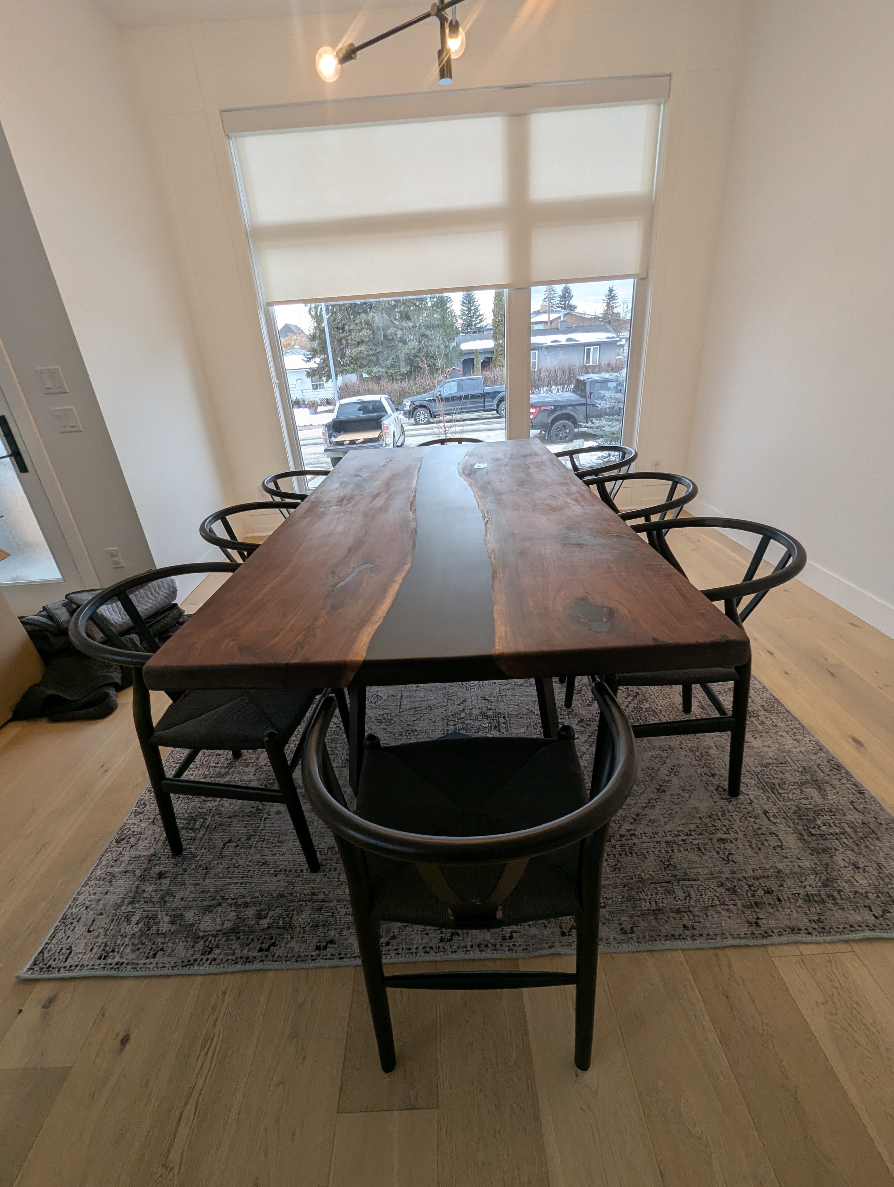 Black epoxy river walnut dining table with wishbone chairs and large windows