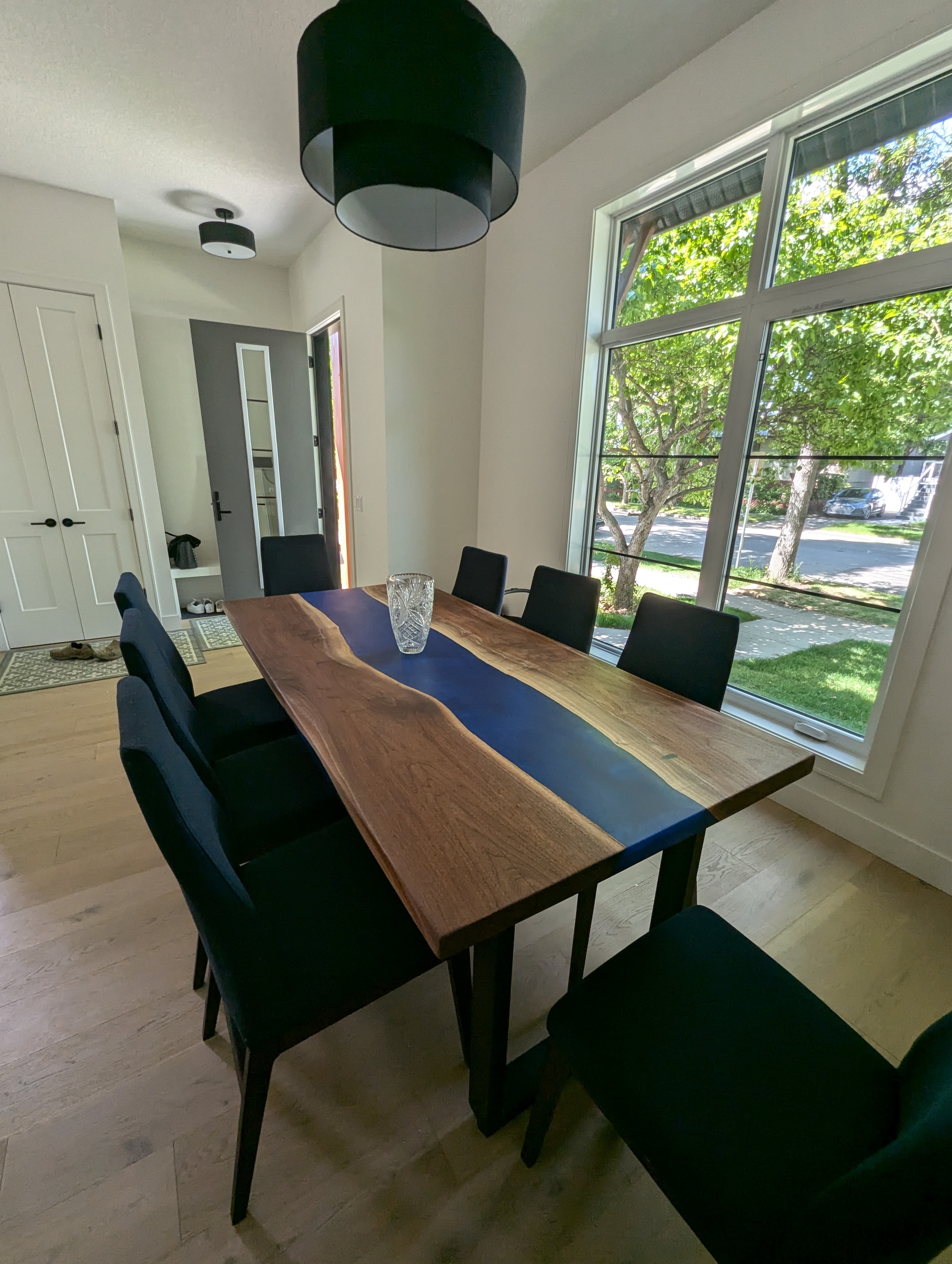 Deep blue epoxy river walnut dining table with black chairs and floor-to-ceiling windows