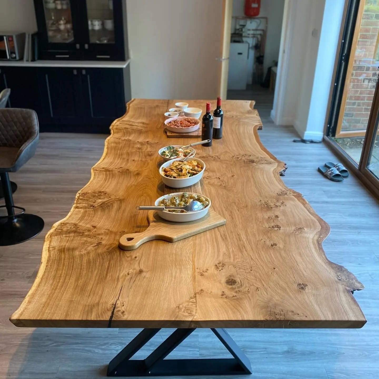 Live edge oak dining table styled with food and wine — Z-base legs in bright modern kitchen