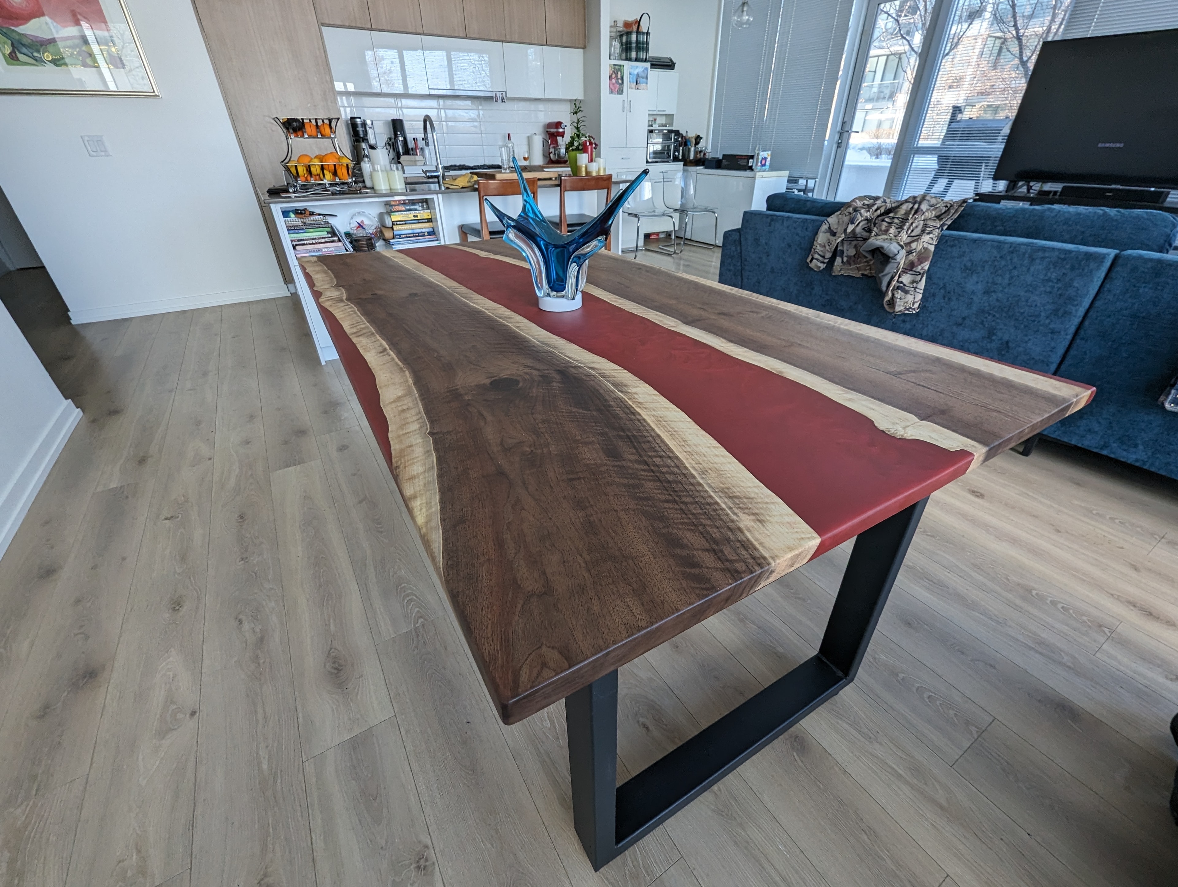 Live edge walnut red epoxy river dining table with black U-base in bright condo