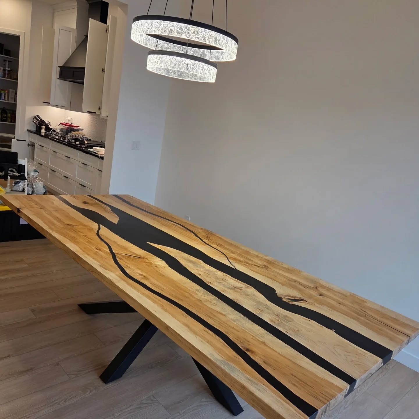 Massive maple black multi-river epoxy dining table with X-base under triple ring chandelier — Calgary home kitchen
