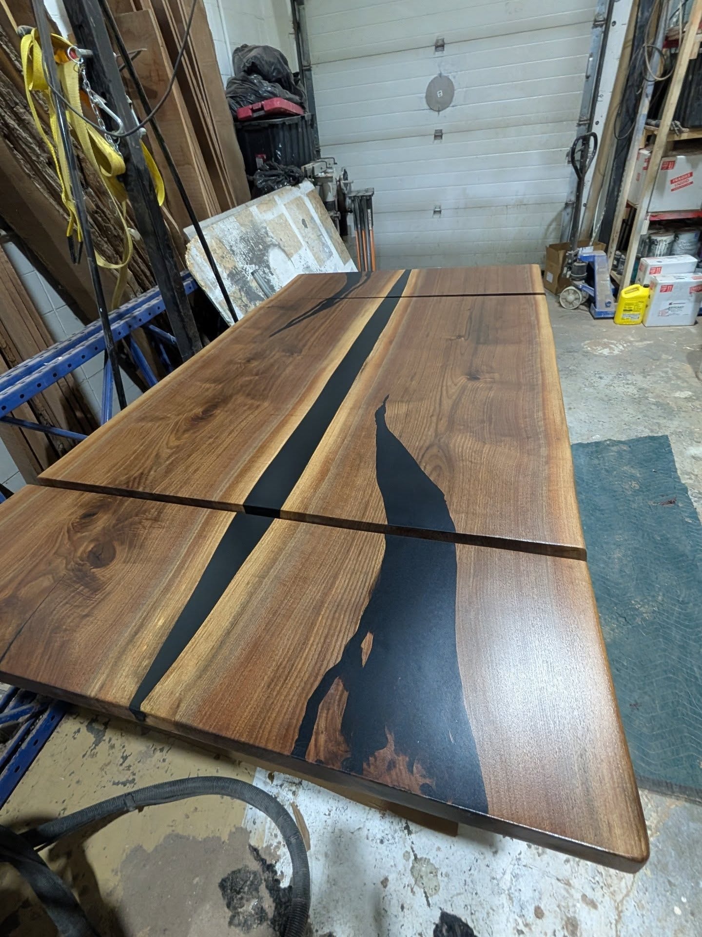 Live edge walnut triple-slab black epoxy river dining table — overhead shop view at Calgary Wood Works