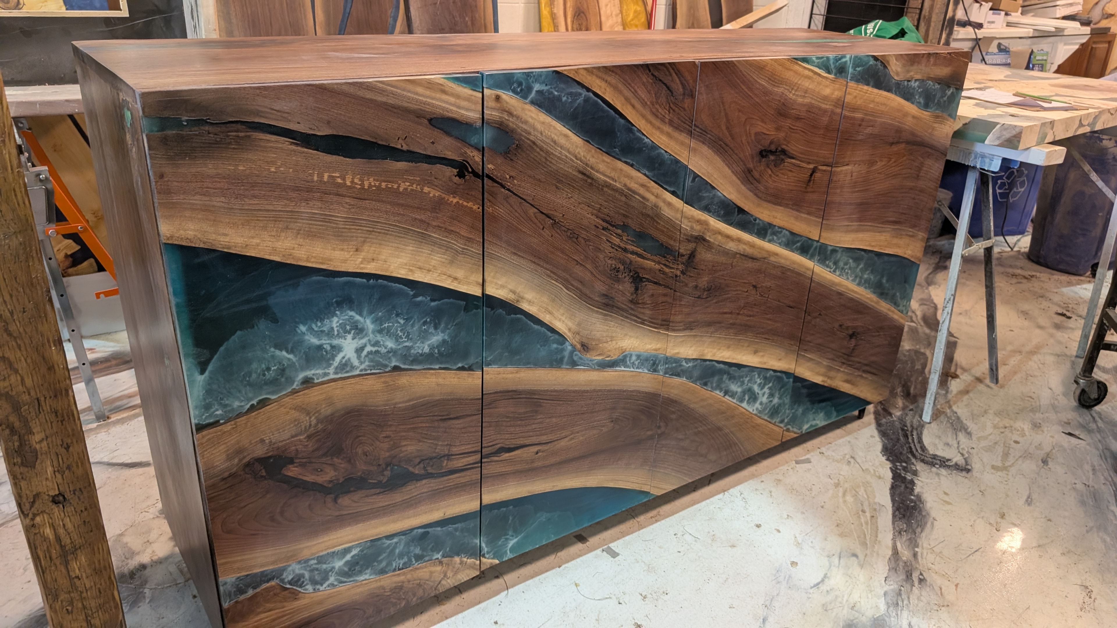 Custom walnut hutch with teal ocean epoxy river doors — wide angle shop view, Calgary Wood Works