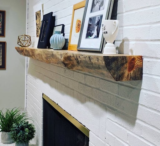 Reclaimed wood live edge fireplace mantel on white painted brick styled with art and eclectic decor — Calgary home