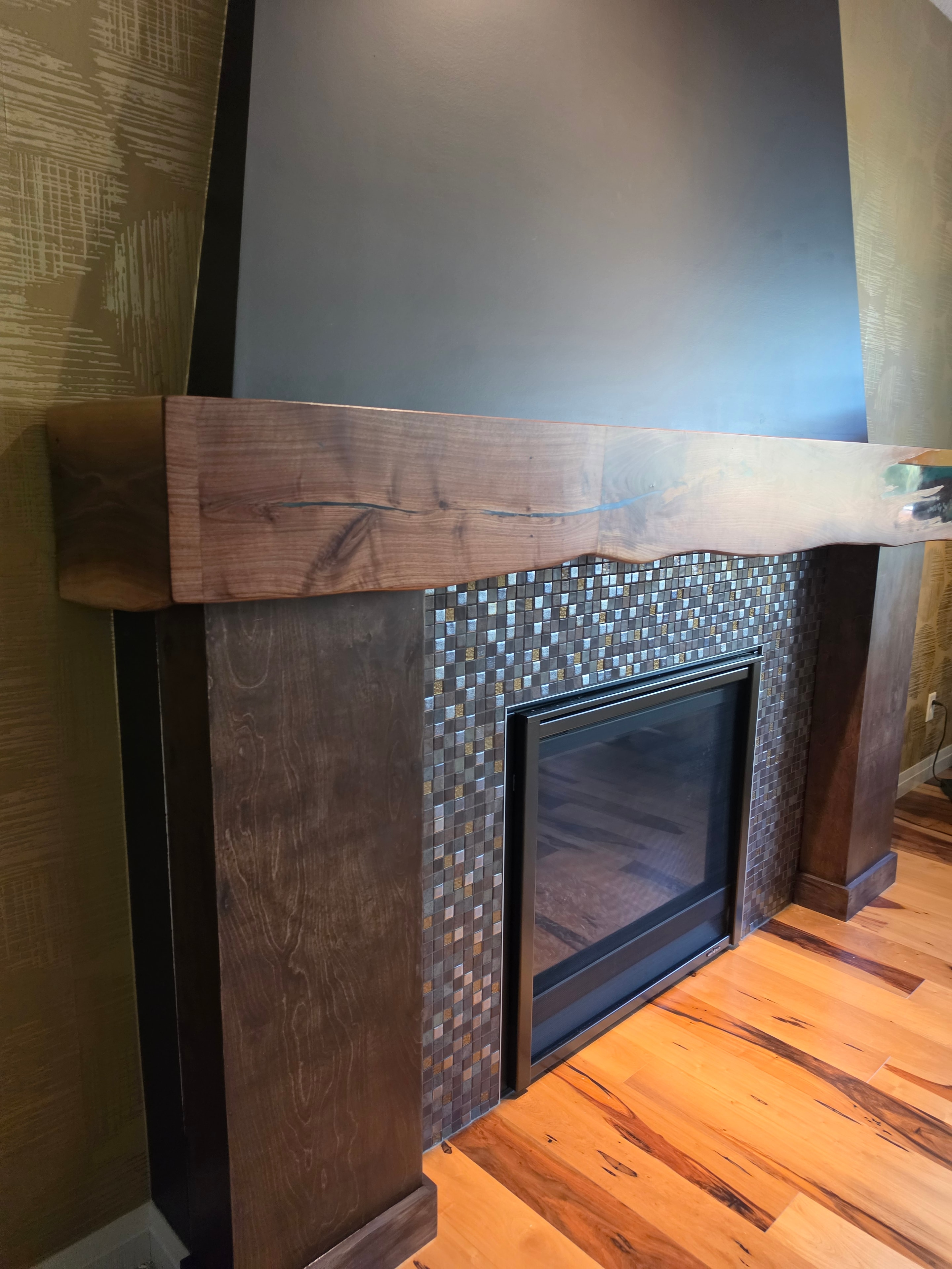 Walnut fireplace surround with teal epoxy and mosaic tile — angled view showing live edge grain — Calgary Wood Works