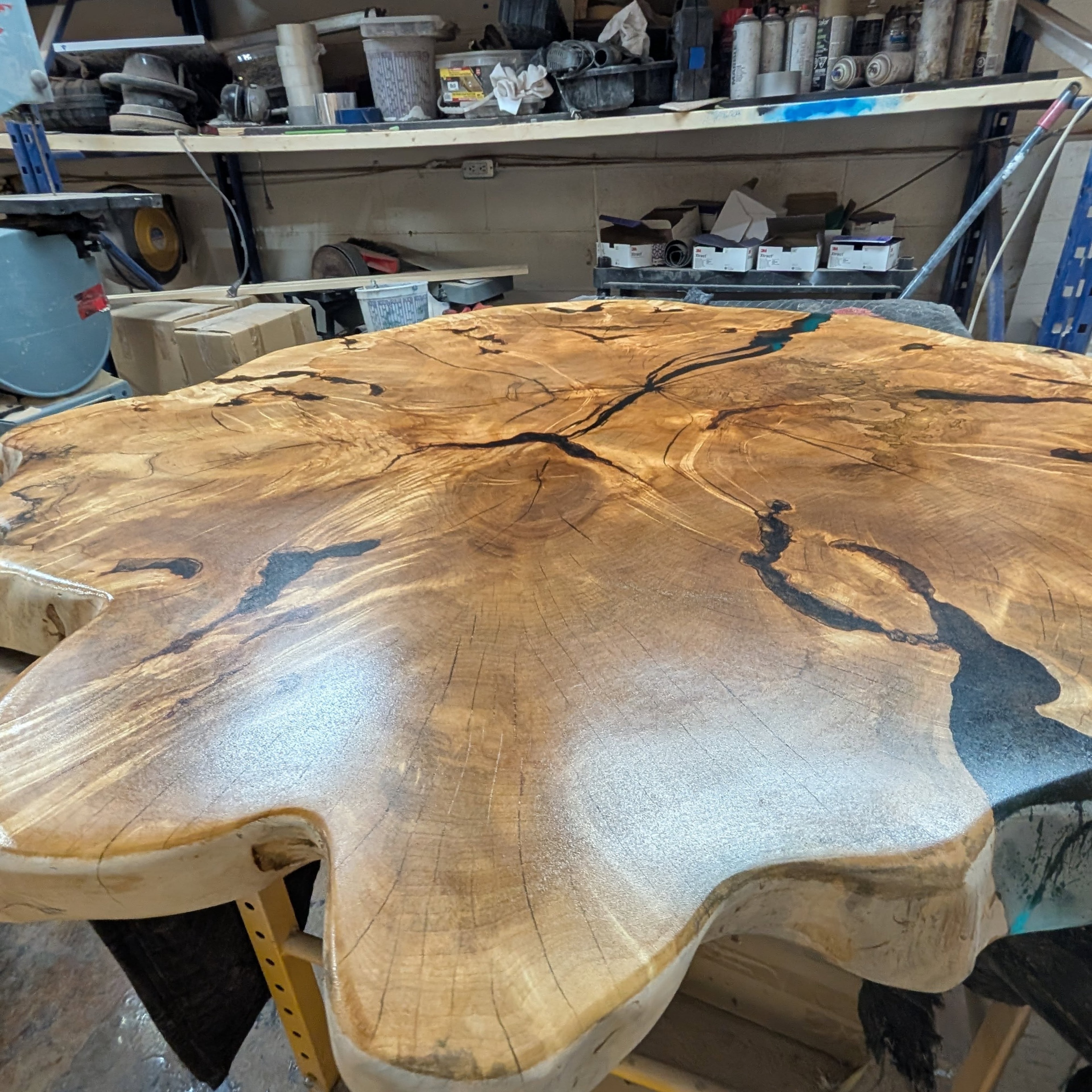 Round live edge slab with black epoxy crack fills in progress — Calgary Wood Works shop