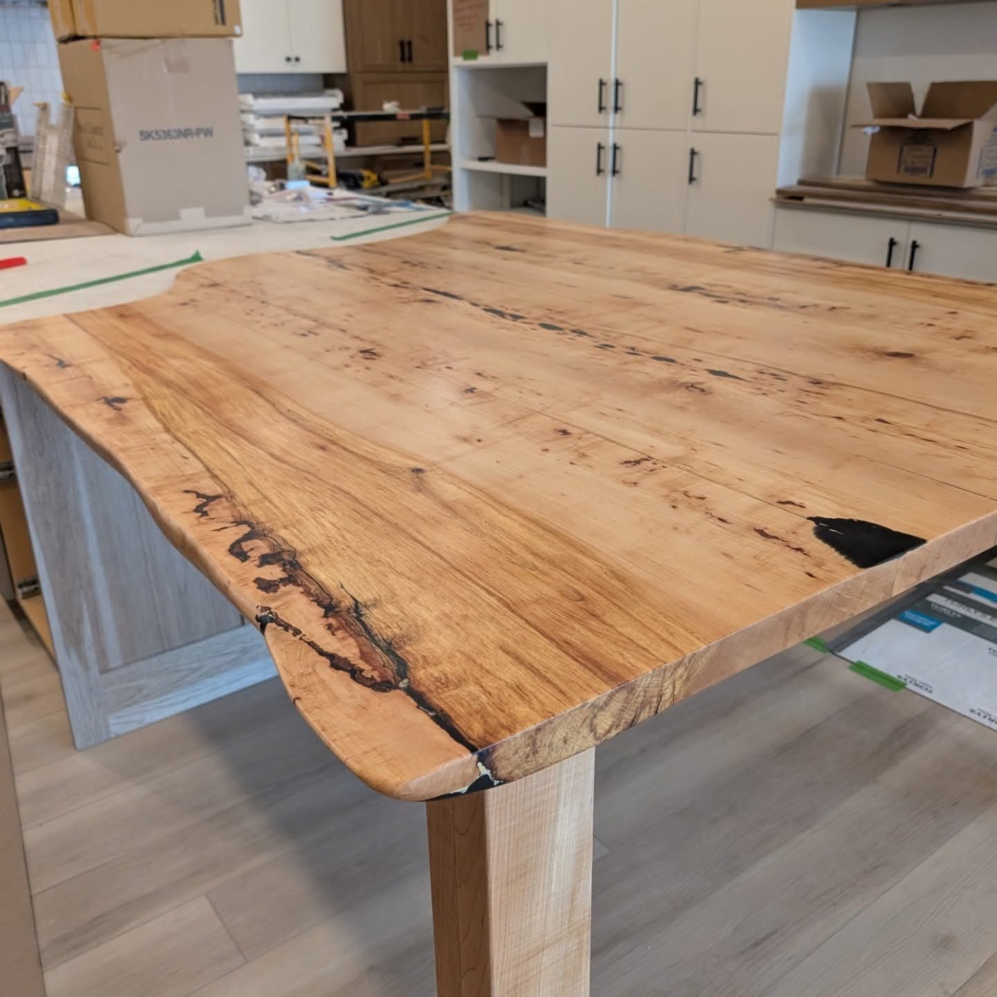 Live edge solid walnut dining table with blue epoxy crack fills beside striped banquette and abstract art